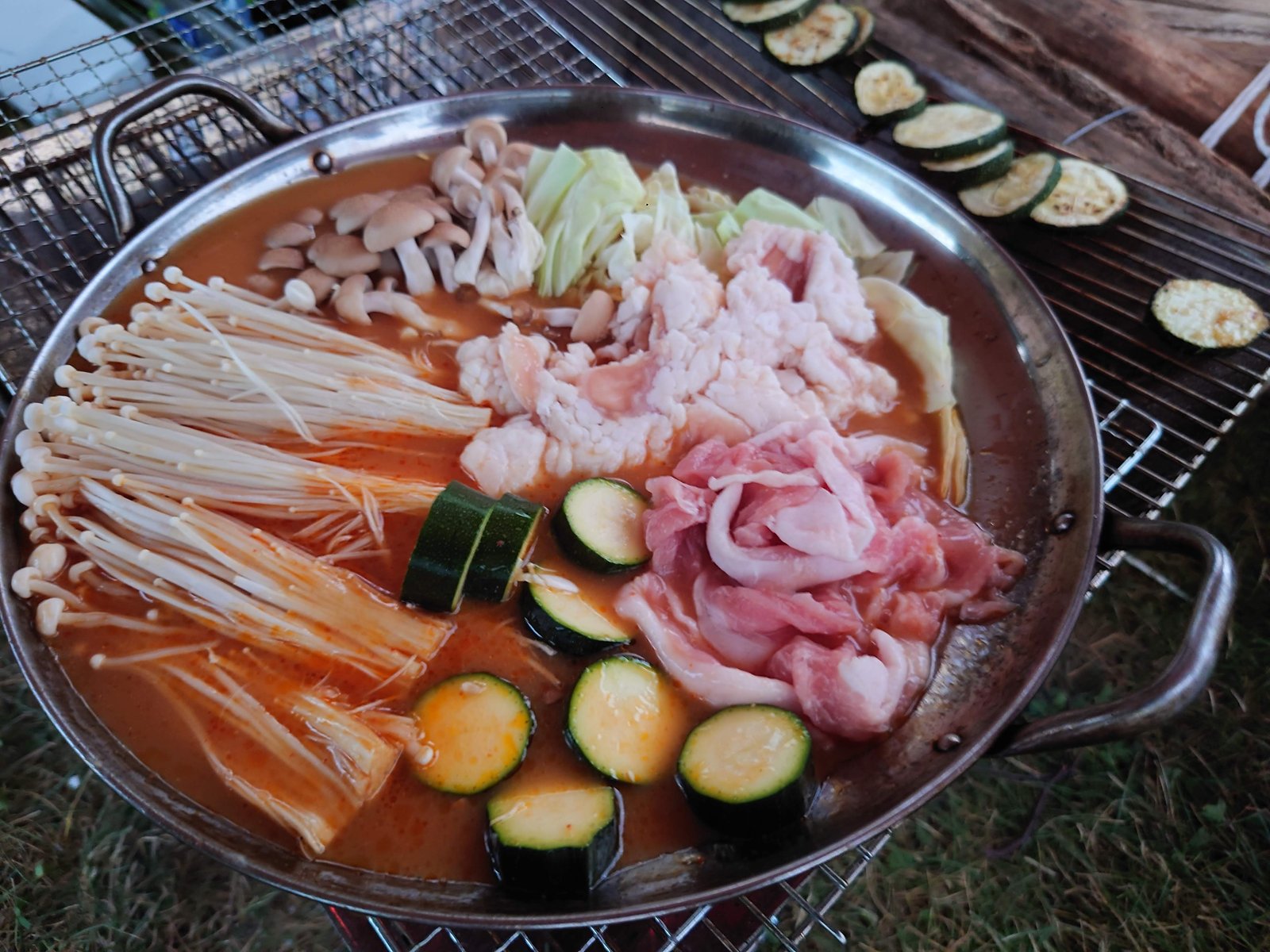 バーベキューコンロの上で煮えるキムチのもつ鍋。豚肉ときのこと夏野菜